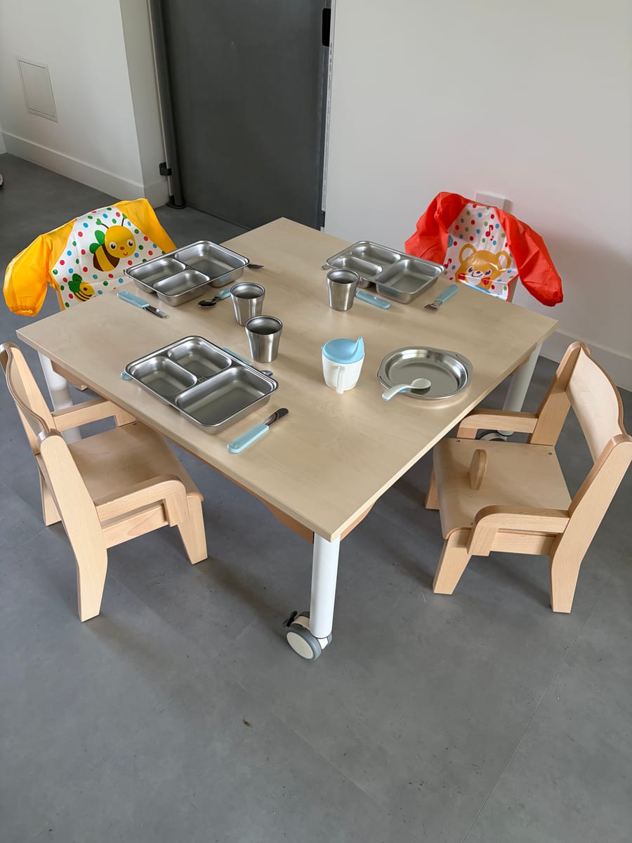 Table de repas préparée avec chaises adaptées, vaisselle et couverts pour les enfants.