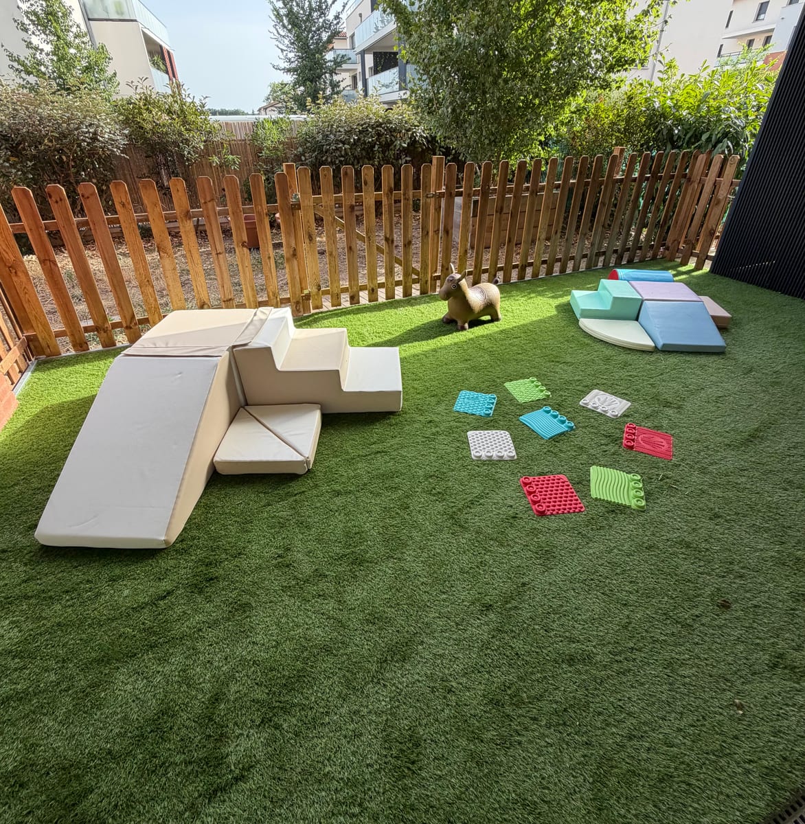 Terrasse extérieure sécurisée avec tapis synthétique, modules de motricité et jeux.